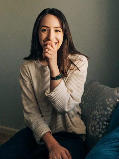 Photo portrait of Belqise, looking at the reader, covering her mouth as she laughs.