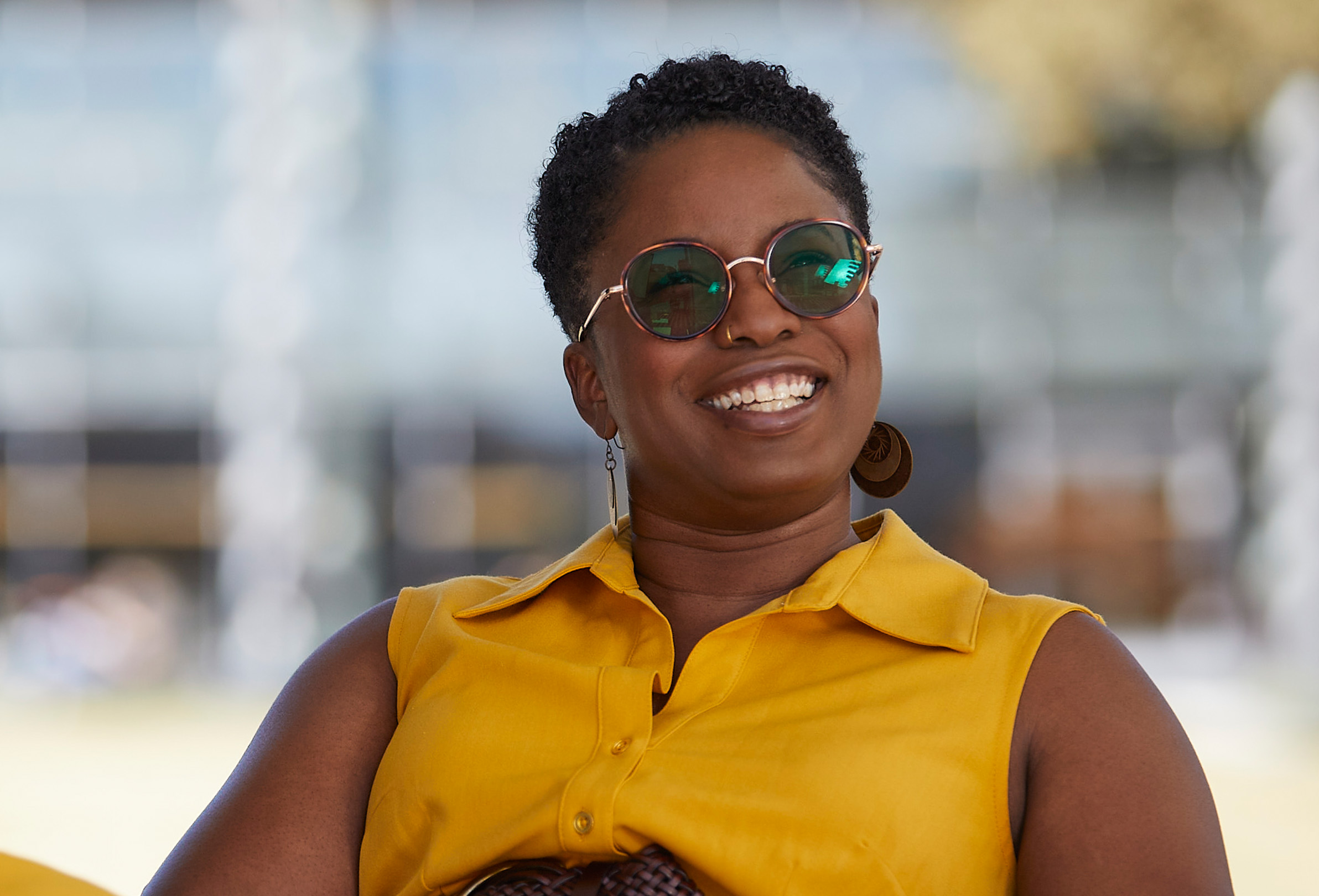 An Apple employee smiling and sitting outside with sunglasses on.