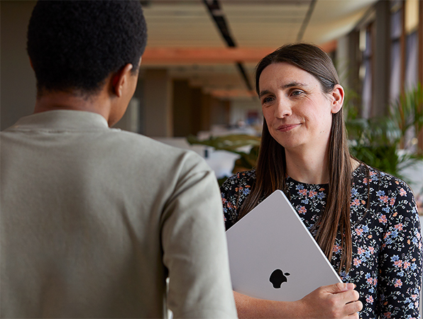 Two Apple colleagues standing while in conversation, one holding a MacBook.