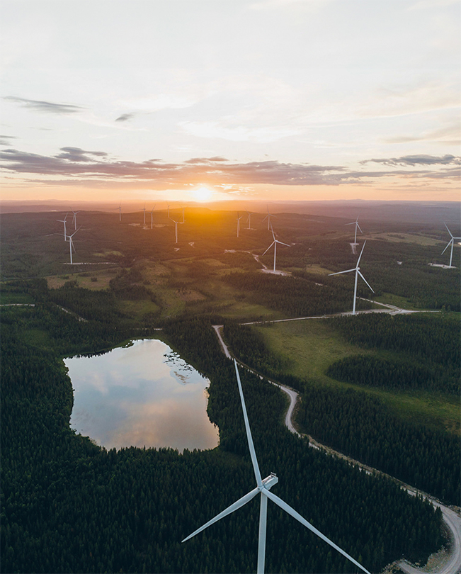 A series of energy-producing wind turbines, arrayed across a verdant countryside, shown from above.