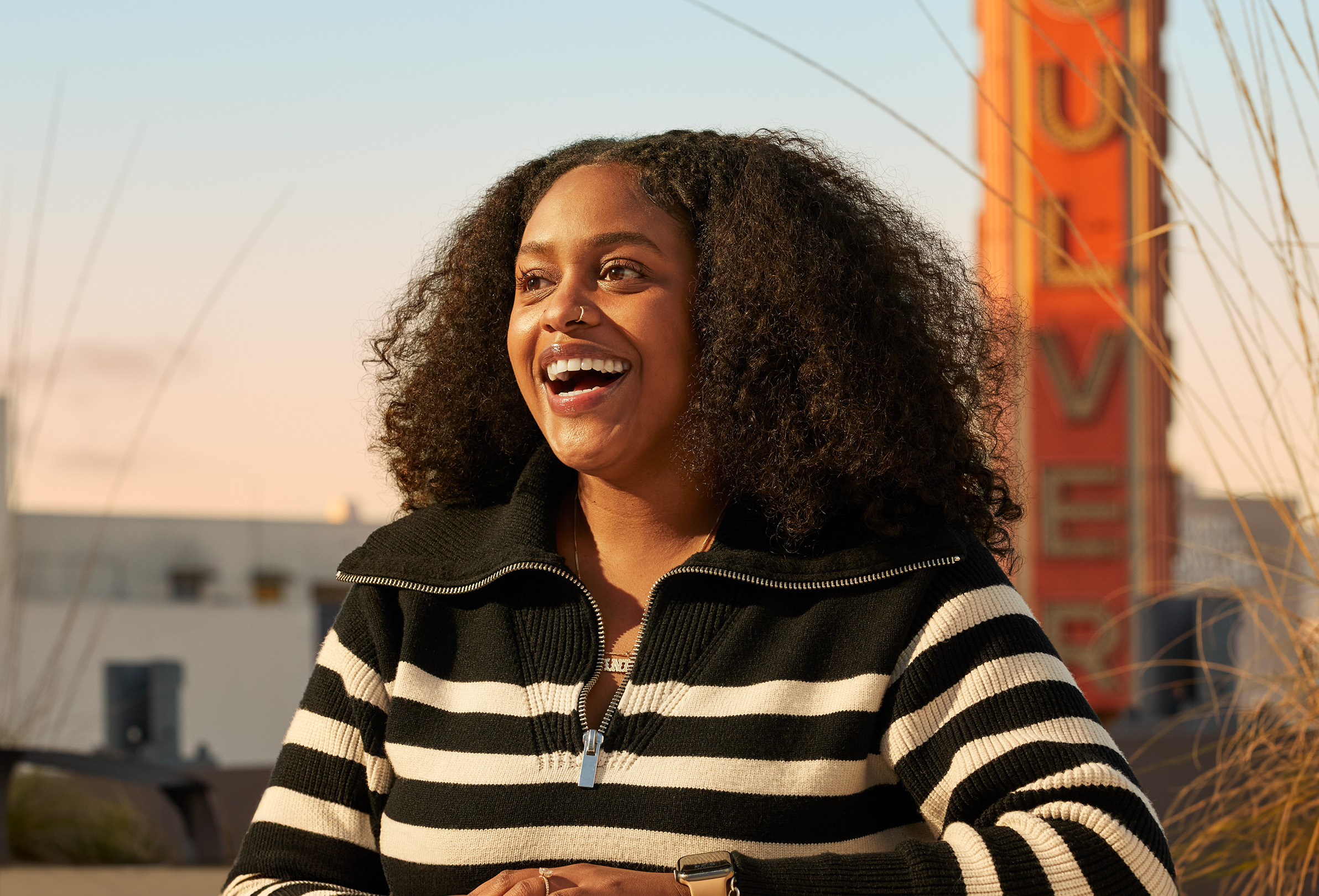 An Apple employee sitting outside on the office roof patio, looking off camera and laughing.