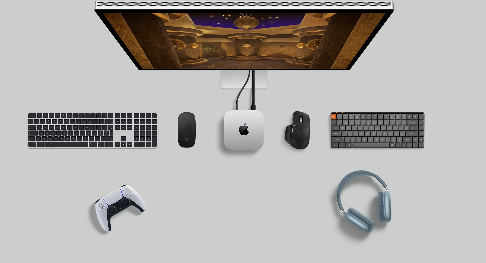 Vista desde arriba de un Mac mini color plata sobre un escritorio, con un monitor, teclados inalámbricos, dos mouse inalámbricos, un control para jugar y unos AirPods Max