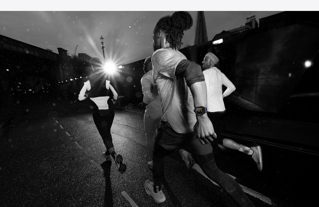 Cuatro personas que llevan un Apple Watch salen a correr por la ciudad de noche.