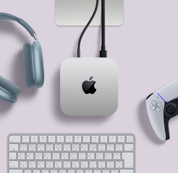 シルバーのMac miniを上から見た図。2本のコードが背面のポートにつながれている。近くにはブルーのAirPods Max、シルバーのMagic Keyboard、ワイヤレスゲームコントローラがある