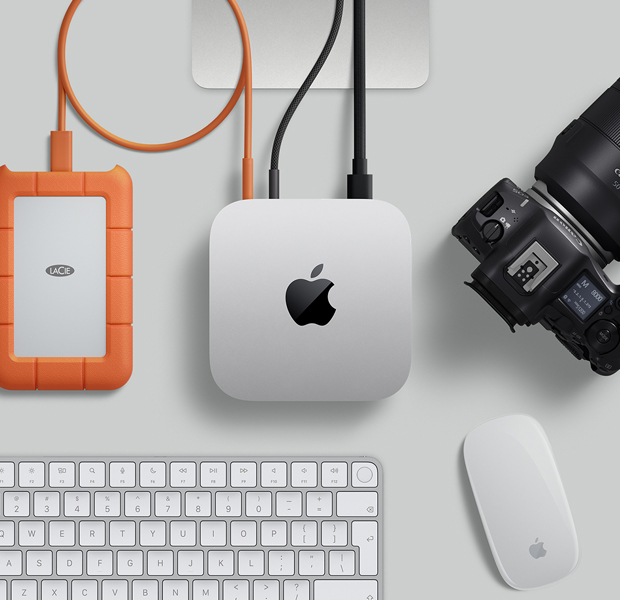 Top view of silver Mac mini, with two cords plugged from the back ports into a display monitor, next to a black Magic Mouse and black Magic Keyboard