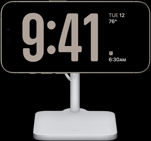 An iPhone 15 Pro in StandBy showing a full-screen clock along with the date, the temperature, and the next alarm